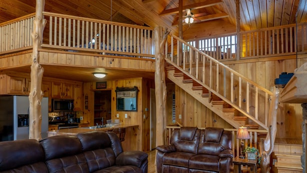 A spacious wooden cabin with a dining area, kitchen, and a staircase connecting two levels. - Secluded Log Cabin, Mountain Top, Hot Tub, Pool Table, 5 Miles From Downtown (Hot Springs)