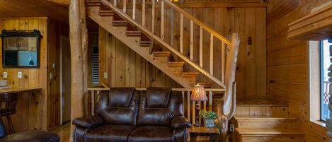 A wooden interior with a staircase, leather sofa, and a lamp.