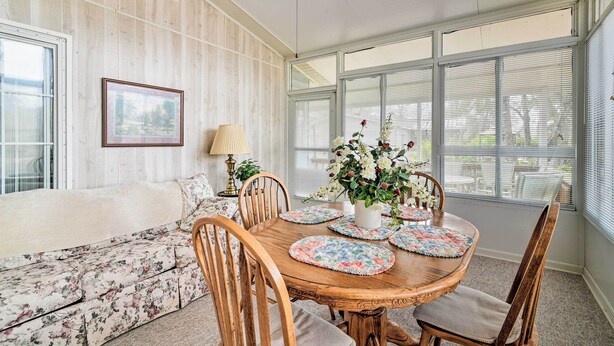 A dining area with a wooden table, floral sofa, and a view of the outdoors through large windows. - Fishing Paradise w/ Deck On Suwannee River (Branford)