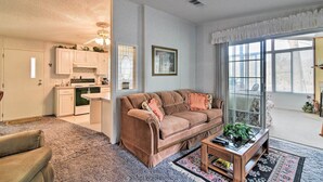 A living room with a brown sofa, a coffee table, and a rug. There is a kitchen in the background with white cabinets and a stove. - Fishing Paradise w/ Deck On Suwannee River (Branford)