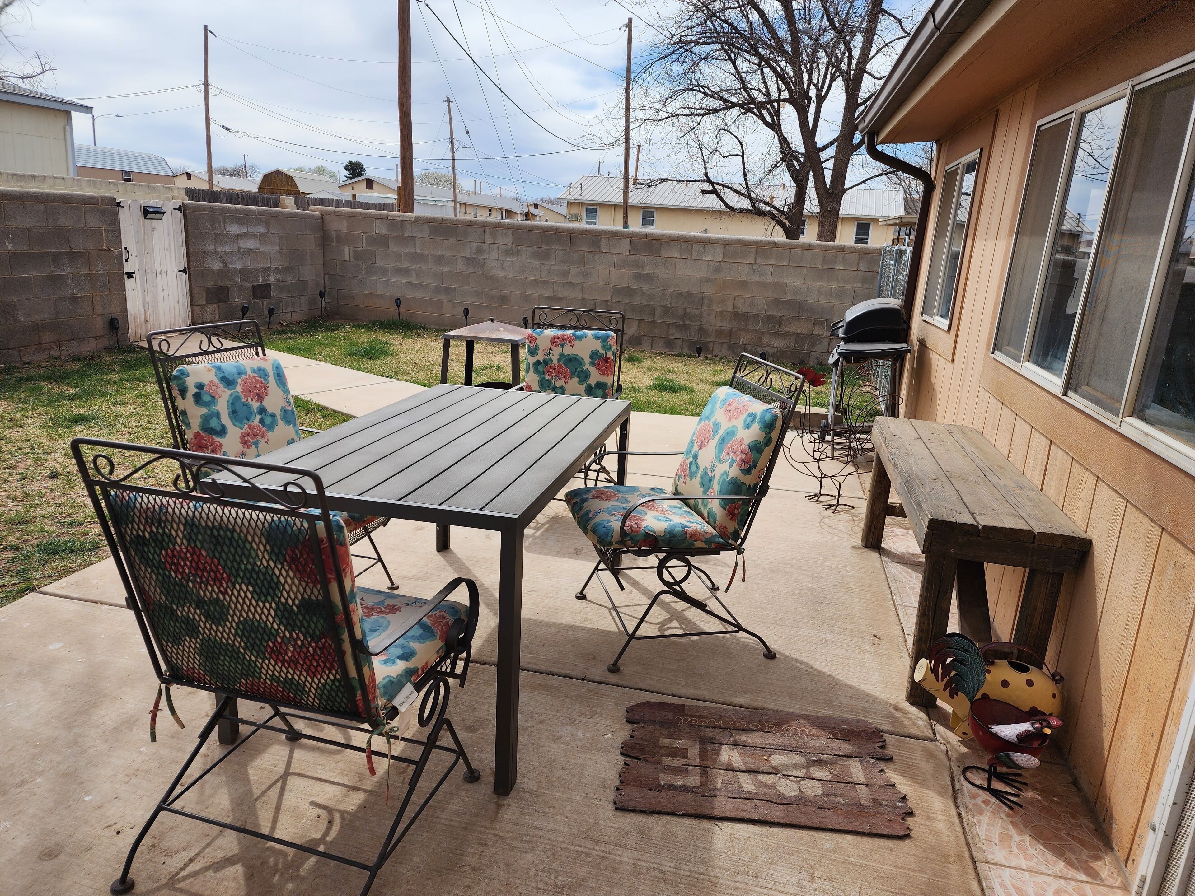 An outdoor patio with a metal table and chairs, a barbecue grill, and a chicken decoration.