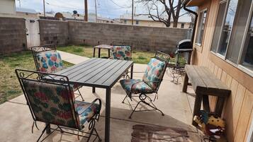 An outdoor patio with a metal table and chairs, a barbecue grill, and a chicken decoration.