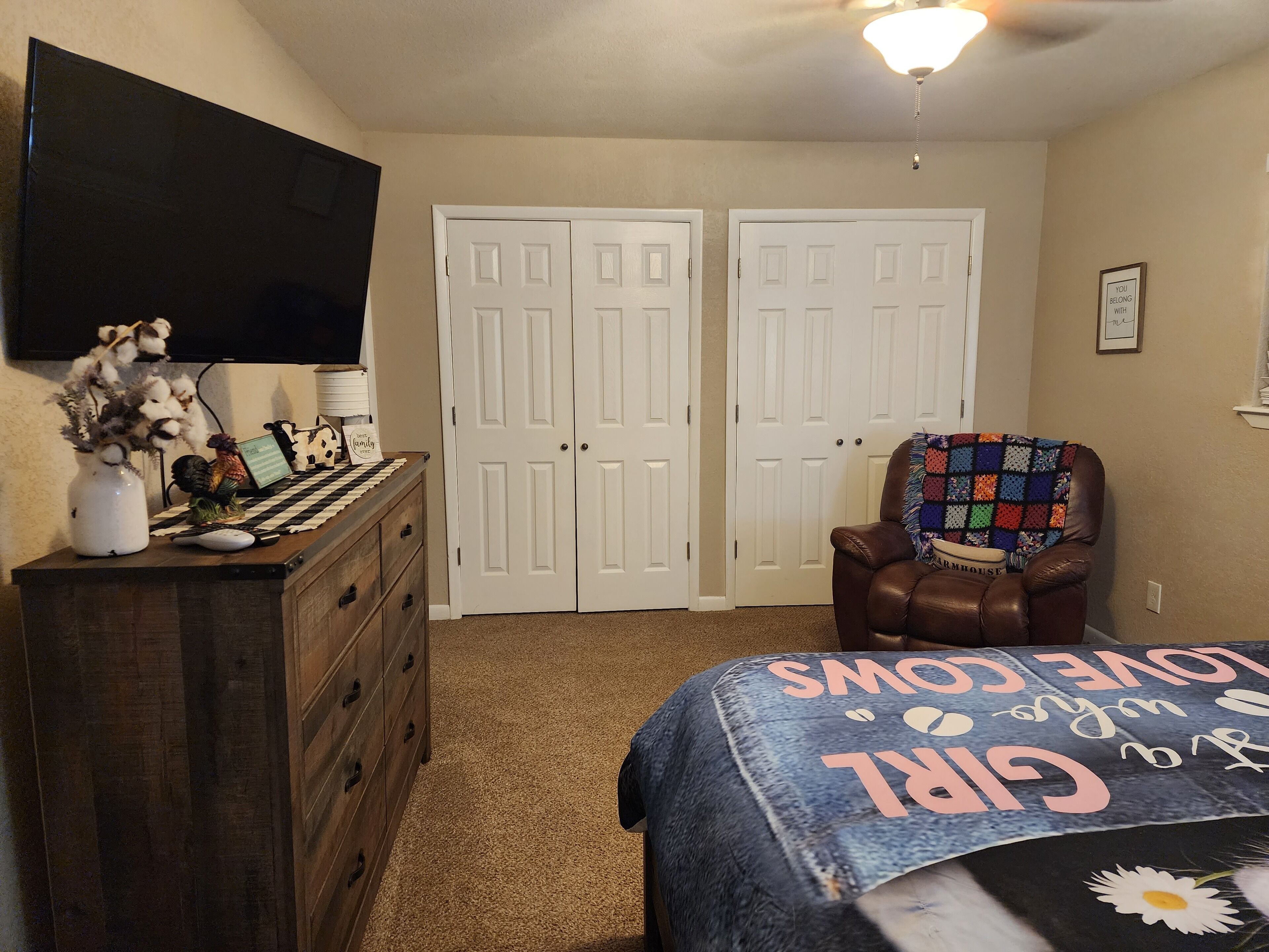 A bedroom with a bed, a dresser, a chair, a television, and a closet.