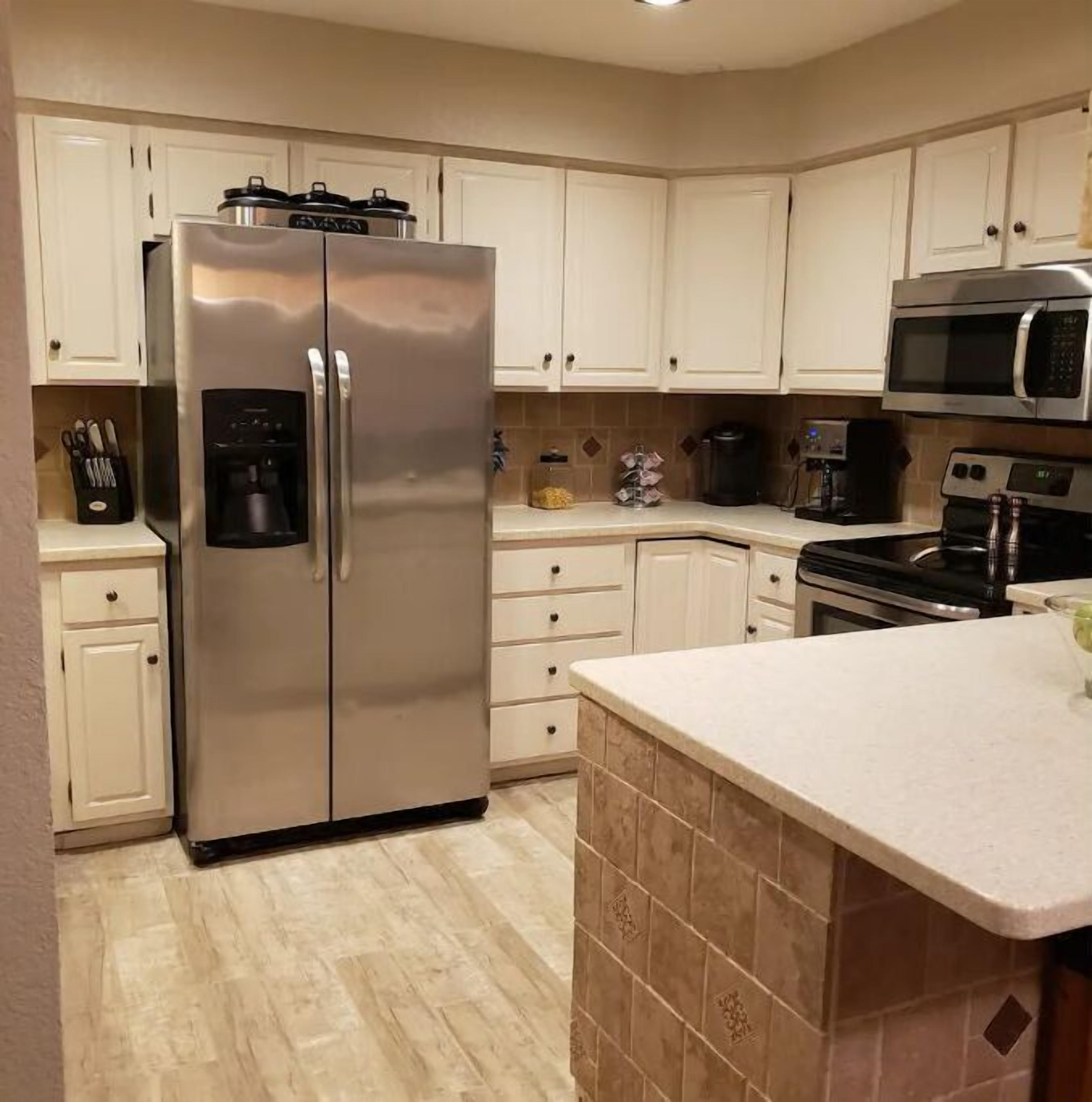 Una cocina con un refrigerador de acero inoxidable, gabinetes blancos, un microondas y una cafetera.