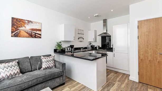 A modern kitchen with white cabinets, a central island, and a grey sofa with patterned cushions.