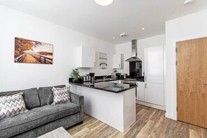 Una cocina moderna con armarios blancos, una isla central y un sofá gris con cojines estampados.
