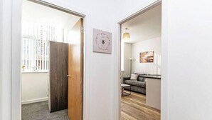 A hallway leading to a living area with a sofa, a small table, and a framed picture on the wall.