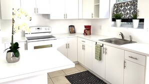 A modern kitchen with white cabinets, a stove, a sink, and a window with plants. - Two Bedroom Apartment, Pool -2 Min  Walk to Miami Design District (Miami)