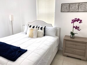 A neatly made bed with white bedding and decorative pillows, a bedside table with a vase of flowers, and a wall-mounted decorative panel. - Two Bedroom Apartment, Pool -2 Min Walk to Miami Design District (Miami)