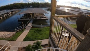 A docked boat with a covered seating area, a grassy area with a pathway, and a railing overlooking a body of water. - Ledges 3BR 2BA, Ground Floor, Water Front, 10x30 slip, 2 Pools and Beach. (Osage Beach)
