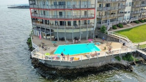 A waterfront building with a swimming pool, outdoor seating, and a view of the water.