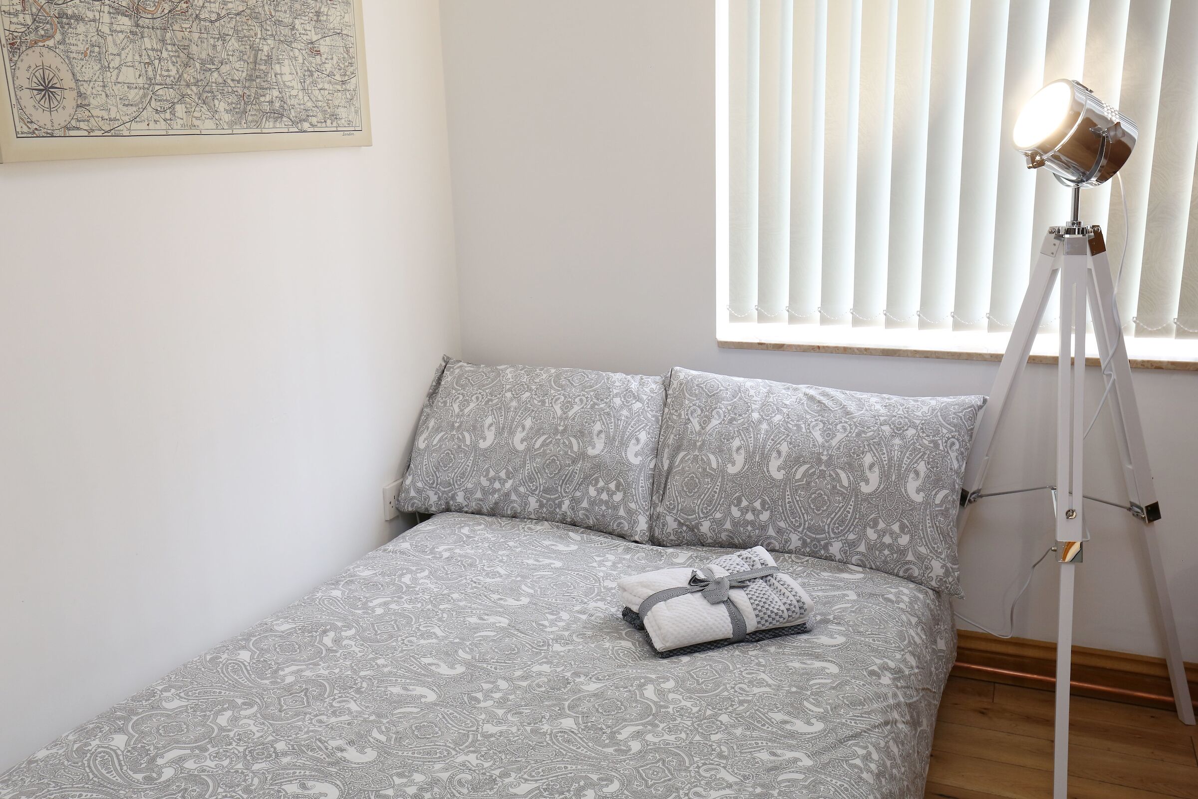 A neatly made bed with patterned bedding, a bedside lamp, and a map on the wall.