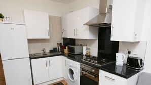 A compact kitchen with white cabinets, a washing machine, a microwave, a stove, and a toaster.