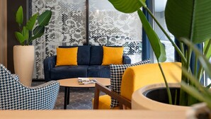 Een moderne woonkamer met een blauwe bank, gele kussens en gestreepte stoelen.