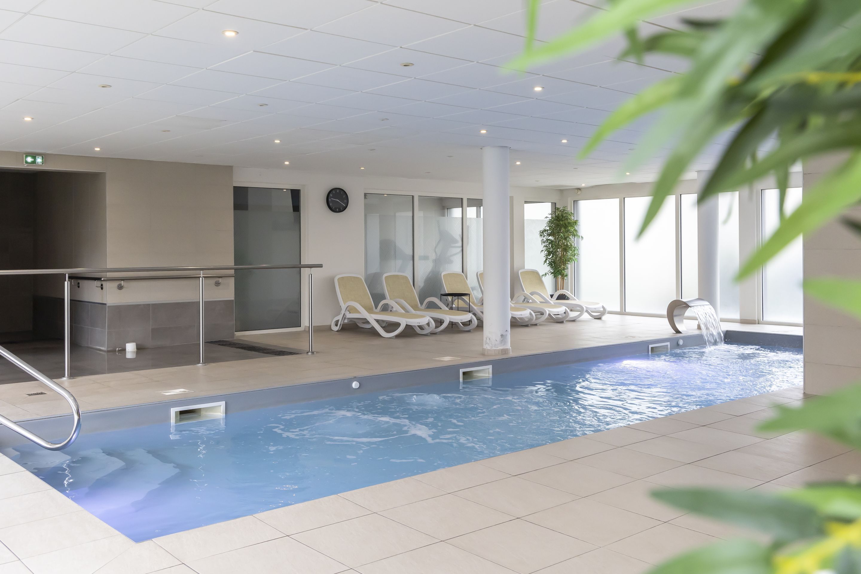 En inomhuspool med solstolar och en vattenfontän.