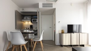A modern living room with a dining area, a TV on a cabinet, and a kitchen in the background.