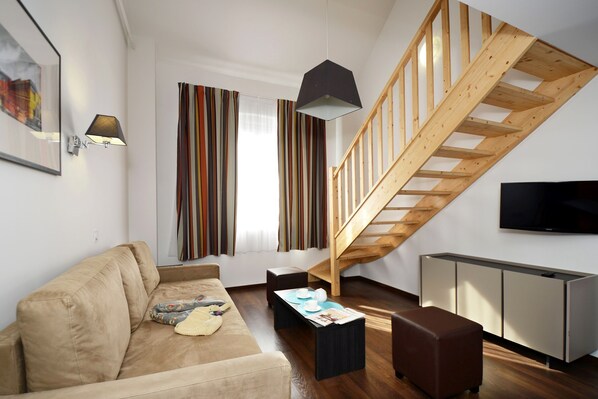 Una sala de estar moderna con una escalera de madera, un sofá, una mesa de centro y un televisor.