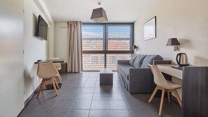 Una habitación de hotel moderna con un ventanal grande, un sofá, un escritorio y un televisor.