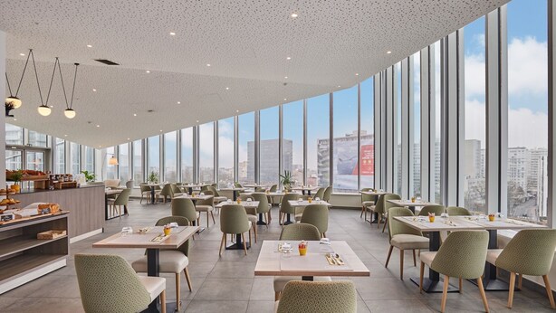 A modern restaurant with high ceilings, large windows, and a city view.