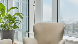A modern room with a large window, a round table, a beige armchair, and a floor lamp.