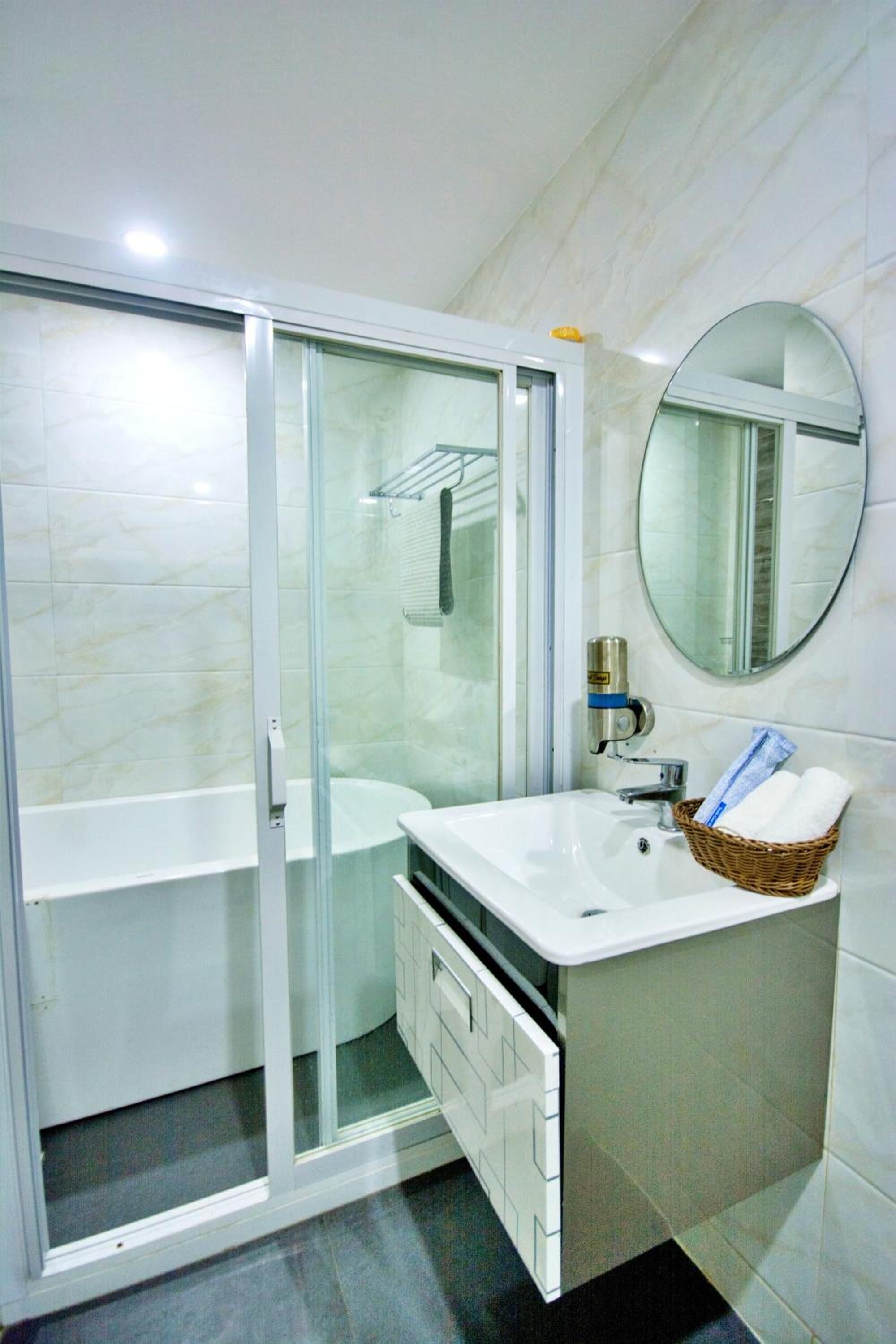 Un bagno con doccia vetrata, lavandino bianco, specchio e cesto in vimini con asciugamani.