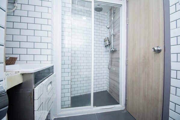 Un baño con paredes de azulejos blancos, una ducha con puerta de vidrio y una puerta de madera.
