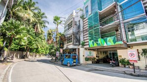 A street view with a blue tuk-tuk parked in front of a building labeled "Emerald Island Hotel Boracay".