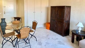 Ett rum med ett matbord i glas, stolar i rotting, ett mörkt träskåp och ett litet sidobord med en lampa.