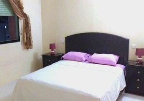 Ein Schlafzimmer mit einem Bett, zwei Nachttischen und einem Fenster mit Vorhängen.