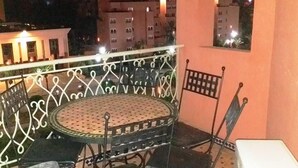 A balcony with a round table and chairs, a white wall, and a view of buildings at night. - Residence Atlas Marrakech 4700 (Marrakech)