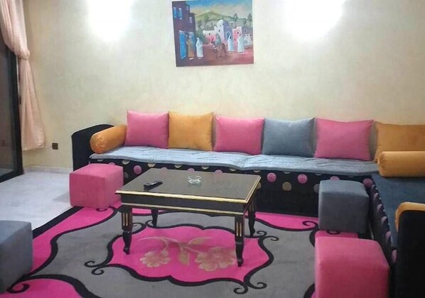 Ein Wohnzimmer mit einer Couch, Poufs, einem Couchtisch und einem Gemälde an der Wand.