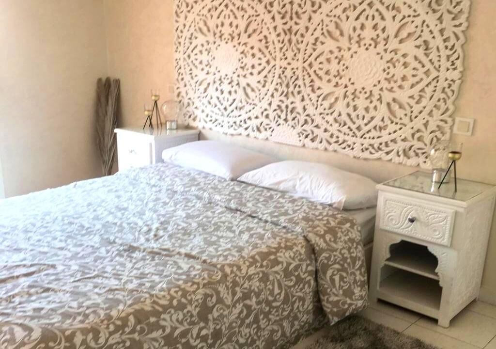 Una camera da letto con una coperta a motivi, un elemento decorativo a parete, un comodino con una lampada e un tavolino.