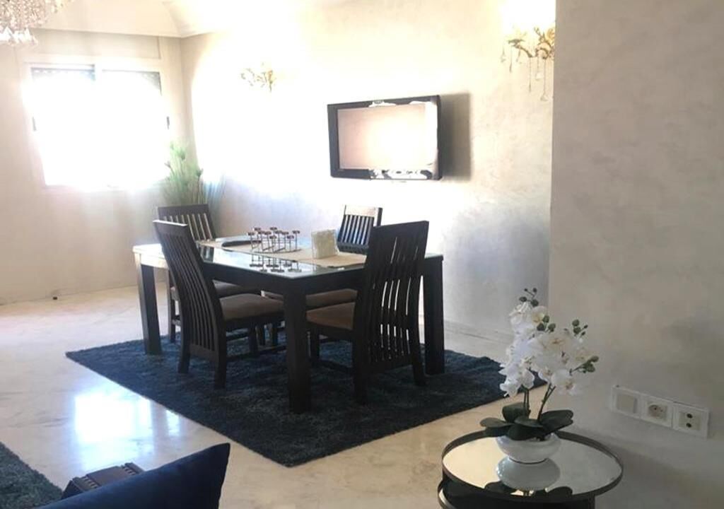A dining area with a table and chairs, a flat-screen TV mounted on the wall, and a potted plant on a side table.