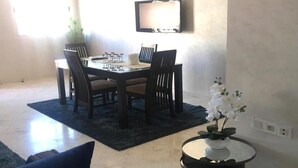Un comedor con una mesa y sillas, un televisor de pantalla plana montado en la pared y una planta en maceta sobre una mesita.