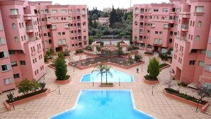A residential complex with pink buildings, a central swimming pool, and landscaped gardens. - Residence Atlas Marrakech 4680 (Marrakech)