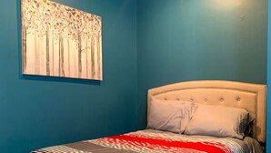 A bedroom with a bed, a painting on the wall, and a blue wall.