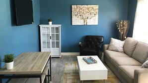 A living room with a blue wall, a white cabinet, a black leather chair, a beige sofa, and a white coffee table.