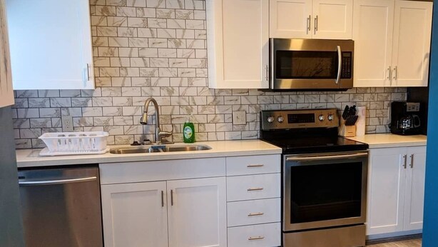 A modern kitchen with white cabinets, a stainless steel dishwasher, a built-in microwave, and a double oven.
