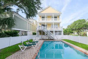 A two-story house with a swimming pool, a covered patio, and a white fence.