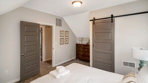 A bedroom with a bed, a dresser, a lamp, and a door. - SPACIOUS home with 5 bedrooms, 4 bathrooms (Cincinnati)