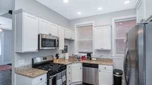 A modern kitchen with white cabinetry, stainless steel appliances, granite countertops, and a wood floor. - SPACIOUS home with 5 bedrooms, 4 bathrooms (Cincinnati)