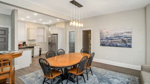 A modern kitchen with white cabinets, a stainless steel refrigerator, and a dining area with a wooden table and chairs. - SPACIOUS home with 5 bedrooms, 4 bathrooms (Cincinnati)