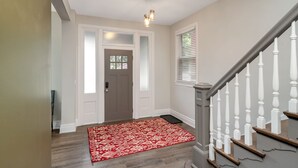 A hallway with a wooden floor, a red patterned rug, a gray door with frosted glass panels, and a staircase with white balusters. - SPACIOUS home with 5 bedrooms, 4 bathrooms (Cincinnati)