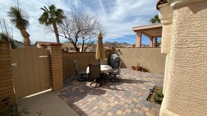 Une terrasse extérieure avec un sol en briques, une table entourée de chaises, un barbecue et un parasol.