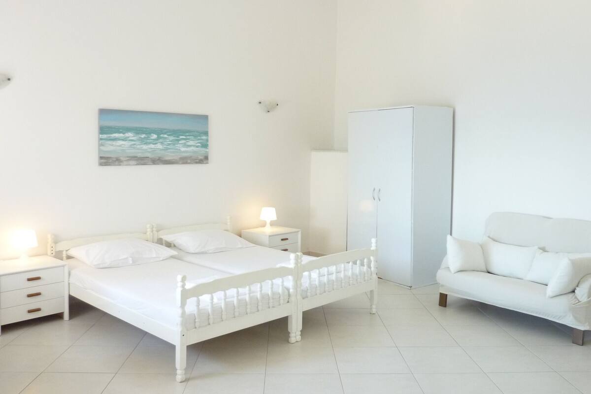 Quarto branco com cama, mesas de cabeceira, um guarda-roupa e um sofá.