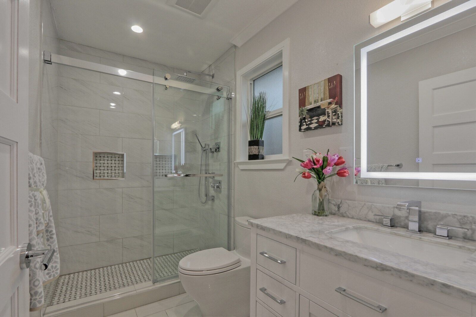 A modern bathroom with a glass-enclosed shower, a white toilet, and a marble vanity with a mirror.
