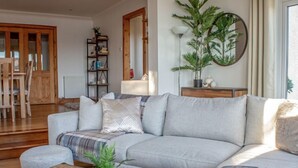 Uma sala de estar moderna com um sofá seccional cinza, uma mesa de centro de madeira com uma planta e um espelho grande na parede.