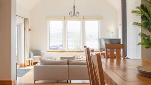 Uma sala de estar moderna com um sofá, mesa de jantar e cadeiras. Há uma janela grande com vista para o exterior.