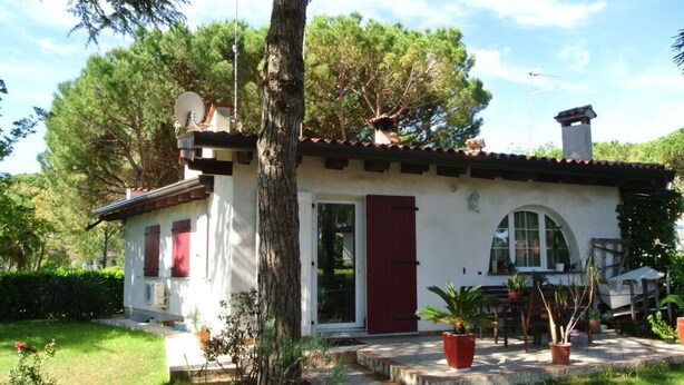 A two-story house with a red door, white walls, and a tiled roof. There is a garden with potted plants and a pathway leading to the entrance.