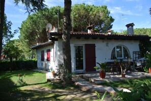 A white building with a red door, surrounded by trees and potted plants.
